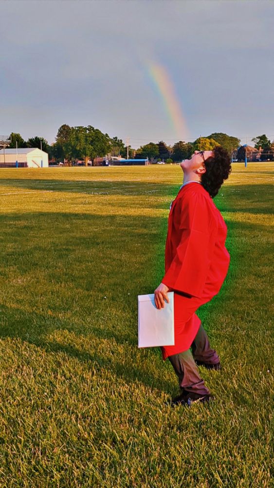 young man in red graduation gown with rainbow ending in his open maw...