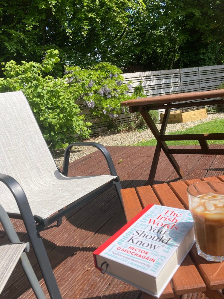 Coffee table with book and iced coffee in foreground and hazel tree and wisteria in background