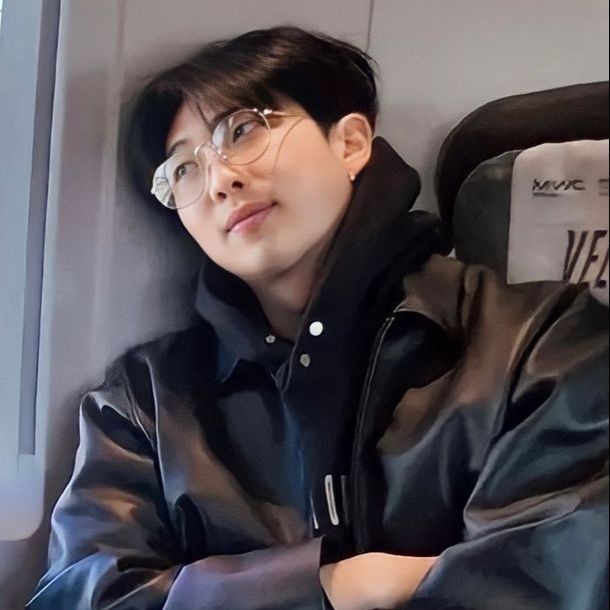 A photo of BTS's Namjoon sitting, looking out the window of a train wearing glasses. The main idea of the post is to make a comparison between the drawing of Snoopy and the photo of Namjoon.