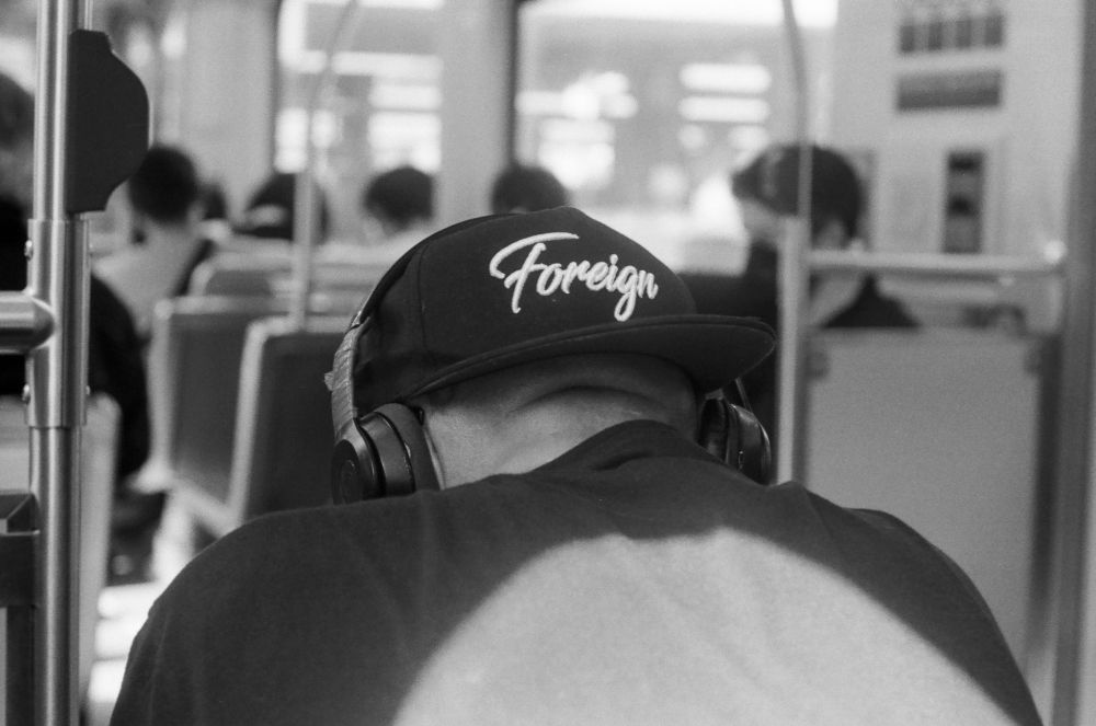 Man in baseball hat that says "Foreign" from behind, on a metro train in Los Angeles, California. Black and white image.