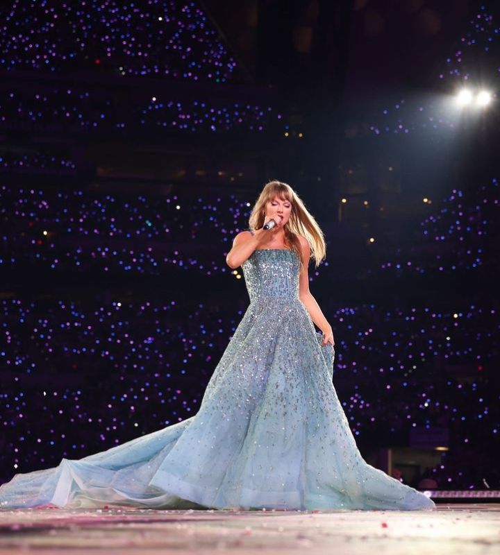 Taylor swift on stage at the eras tour  during speak now set, she's wearing  a blue dress and walking stage