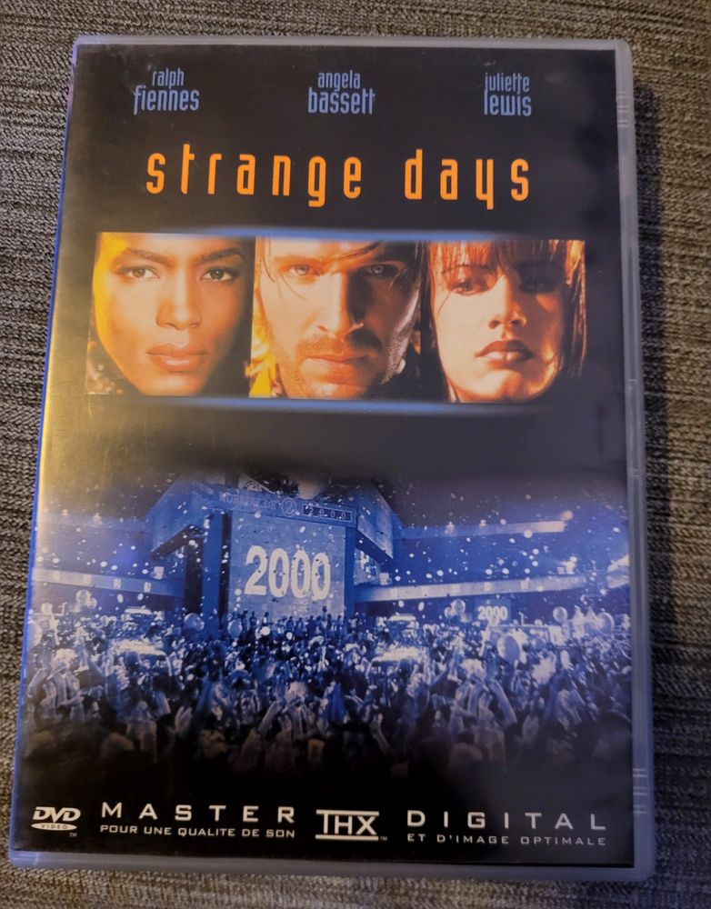 DVD français du film "Strange Days".
Il montre une rue bondée de gens. Scène de nuit. Un panneau géant indique "2000".
Au-dessus : le portrait des trois acteurs principaux : Angela Bassett, Ralph Fiennes, et Juliette Lewis.
