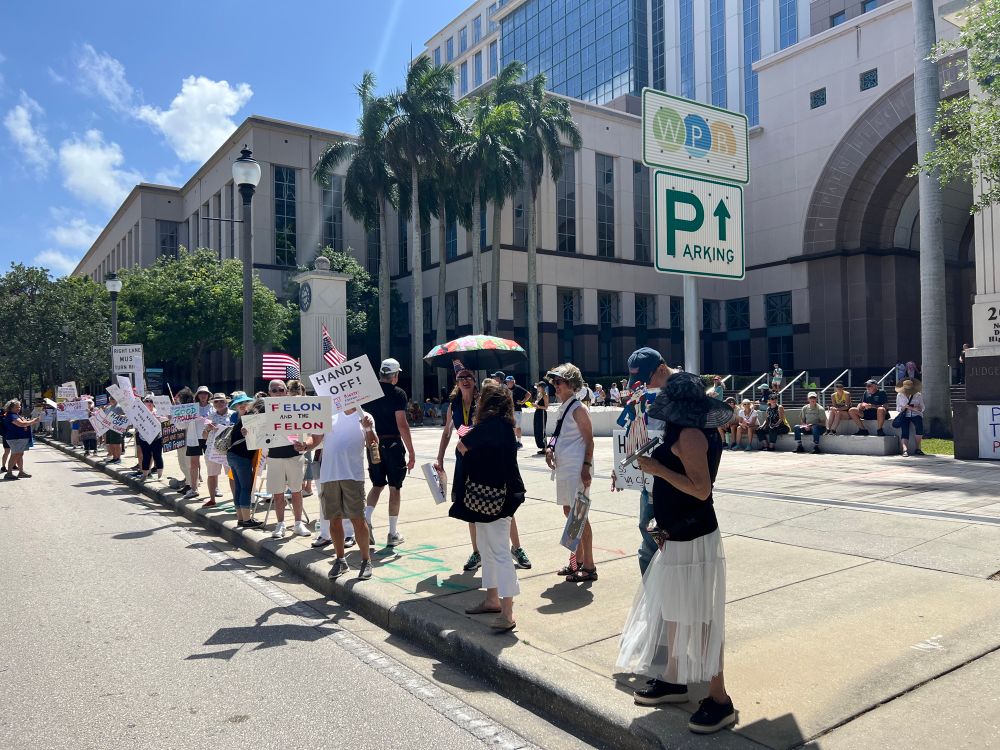 A crowd of protesters with signs stand in front of the County Courthouse in West Palm Beach, Florida. 