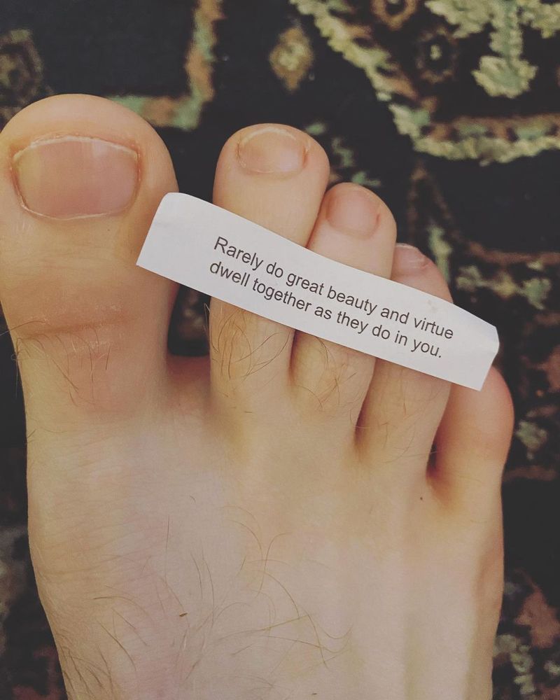 A fortune cookie fortune saying "rarely do great beauty and virtue dwell together as they do in you." The fortune is on top of a fully naked foot