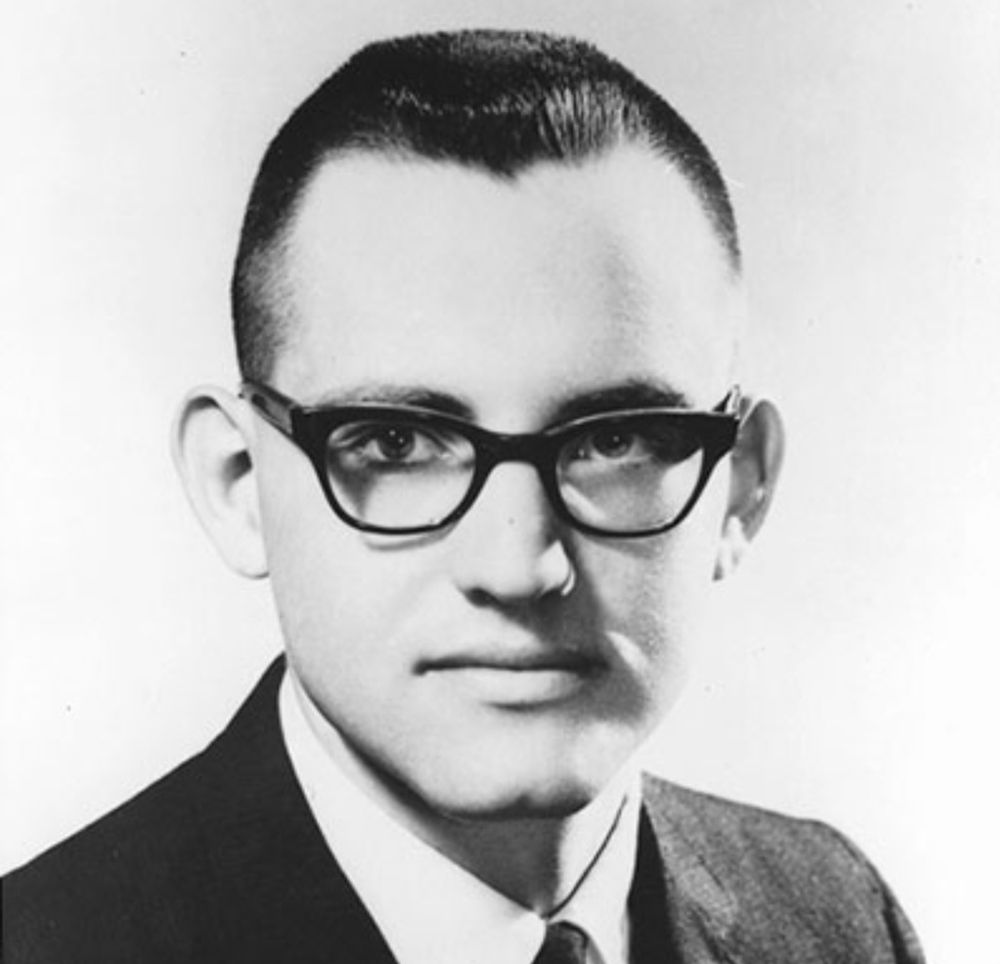 Black and white vintage headshot of Rev. Bruce Klunder. He is a white man in his early 20s. He has very short dark hair,  black glasses, prominent ears, and is wearing a suit and tie.  He is looking directly at the camera with a serious expression. 