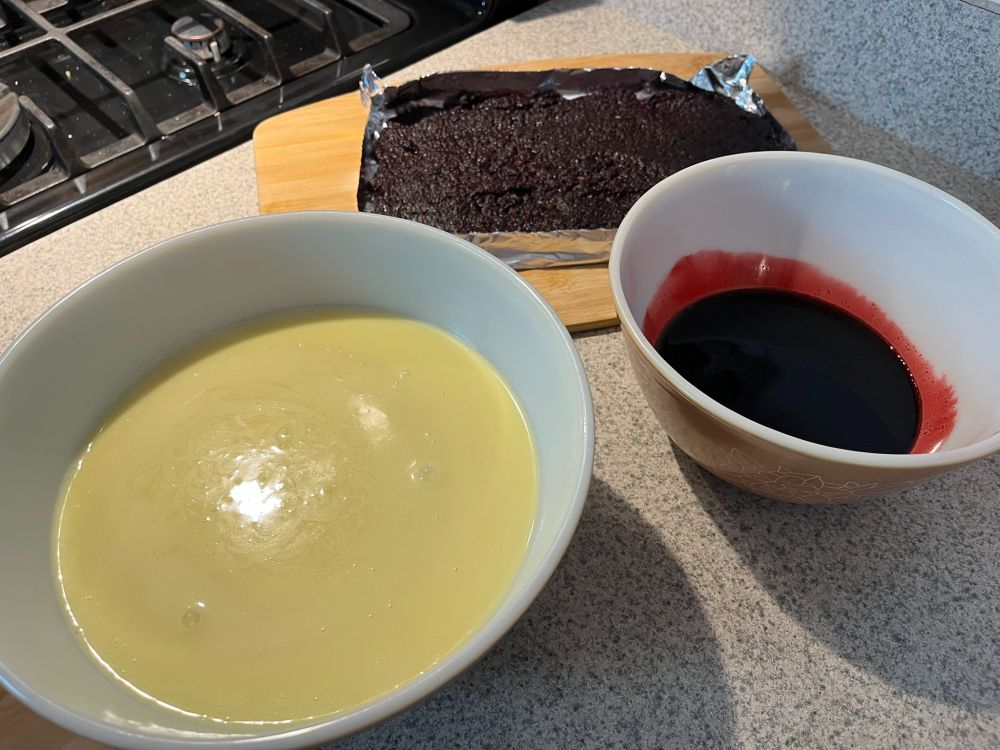 A bowl of vanilla ice cream custard base, another bowl with black raspberry sauce, and a foil tray of the strained-out berries and seeds to be used as a (very crunchy) spread