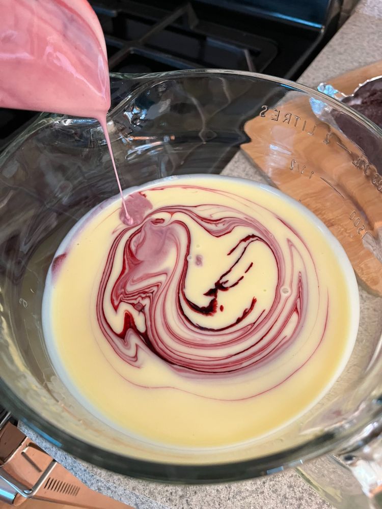 Plain custard ice cream base with black raspberry sauce being drizzled in to create delicious-looking swirl patterns