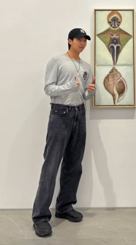namjoon in a grey long sleeve too and black jeans, standing next to a painting of seashells