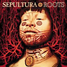 Albumcover Roots von Sepultura. Ein Mensch mit Tätowierungen, vor allem auf dem Unterkiefer schaut entspannt an der Kamera vorbei. Hinter ihm ist ein blutrotes Geflecht aus Wurzeln vor einem schwarzen Hintergrund 