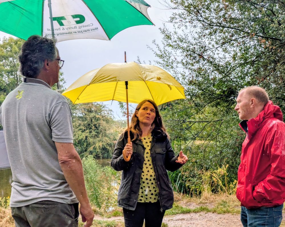 Vikki in Shapwick with National Trust staff members holding an umbrella in the rain.