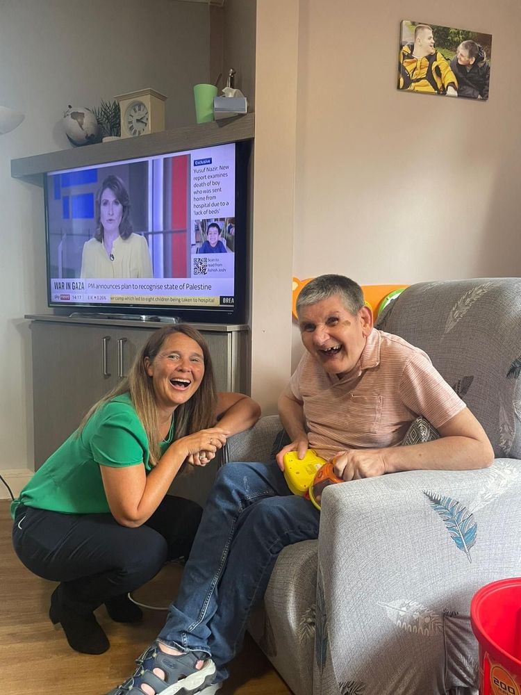 Vikki kneeling next to a resident supported by the charity, both smiling.