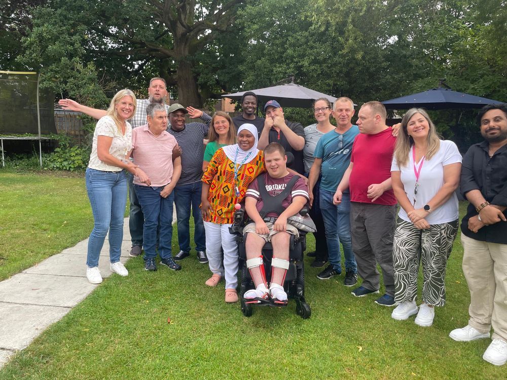  Staff members from Community Integrated Care and people supported by the charity stand outside in the garden, on the grass. The are joined by Vikki Slade. 