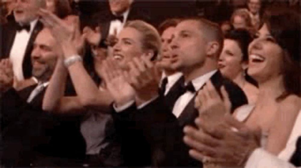 a group of people are applauding in a theatre .