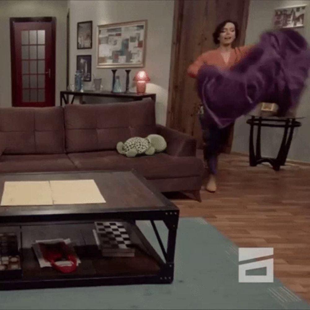 a woman throws a purple blanket in a living room with a tv logo on the floor