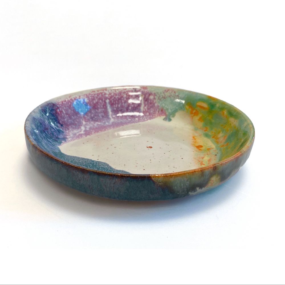 Small dish or plate. It has been dipped in 4 different glazes, making a design with a white triangle in the center surrounded by purple, blue, and green on each side.