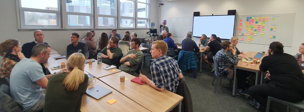 People sitting in a classroom. There are lots of post-its on the whiteboard.