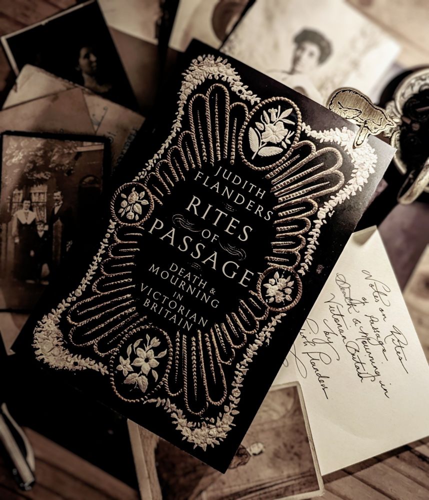 A book called RITES OF PASSAGE: Death and Mourning in Victorian Britain by Judith Flanders. The book is resting on some notes and old Victorian and Edwardian photos.