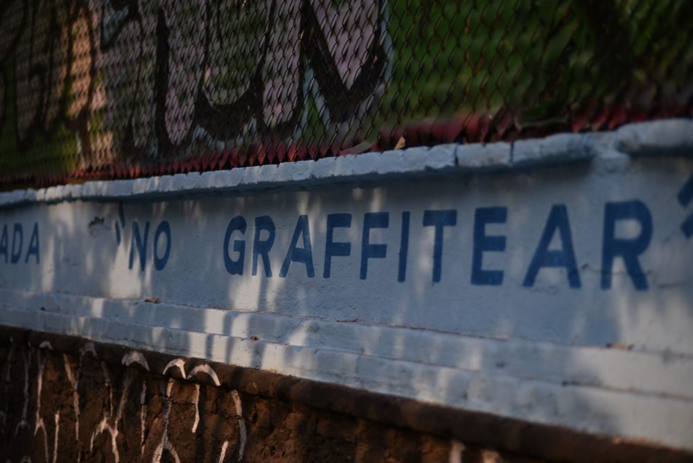 Photo of a wall that has "no graffitear" painted on it, that is absolutely covered in graffiti 