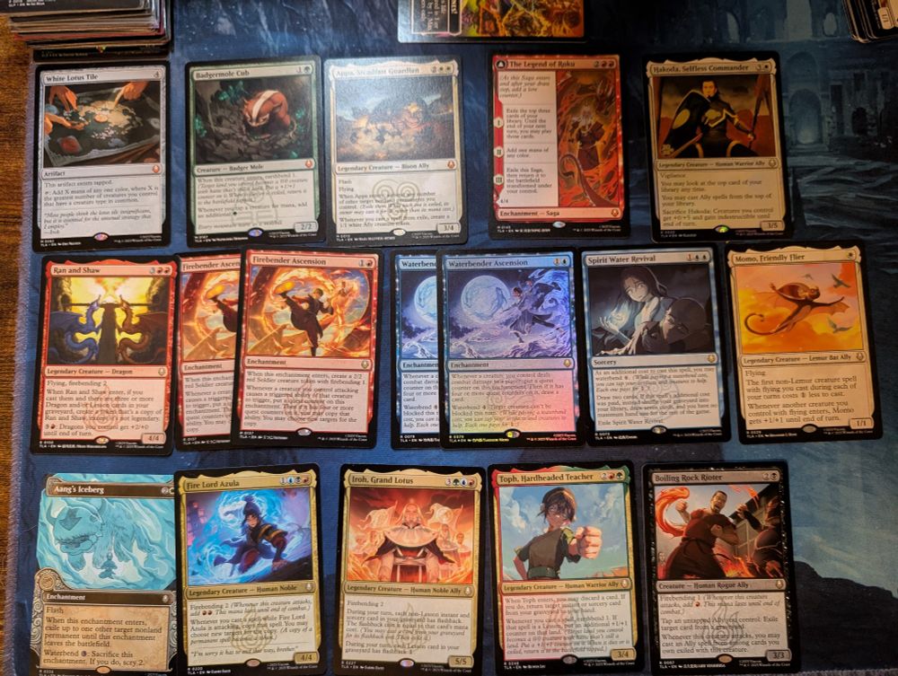 A series of magic cards laid out on a blue playmat.

Left to right:
White Lotus Tile, Badgermole Cub, Appa, Steadfast Guardian, The Legend of Roku, Hakoda, Selfless Commander
Ran and Shaw, Firebender Ascension (x2), Waterbender Ascension (x2, one is foil), Spirit Water Revival, Momo, Friendly Flier
Aang's Iceberg, Fire Lord Azula, Iroh, Grand Lotus, Toph, Hardheaded Teacher, Boiling Rock Rioter