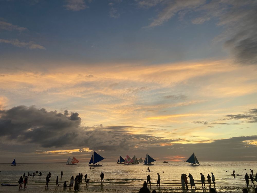 photo of the ocean at sunset with lots of boats and people