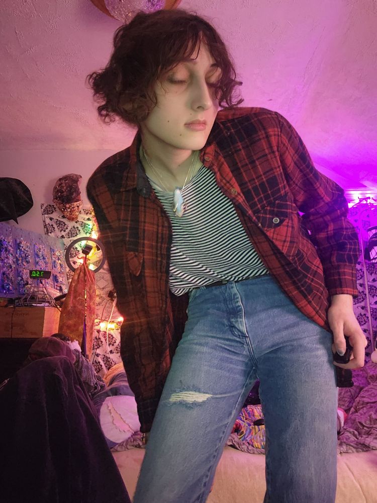 hathaway lour accidentally taking a photo of himself with his eyes closed, he has some scuffed vintage jeans and a striped shirt and our dyke flannel on