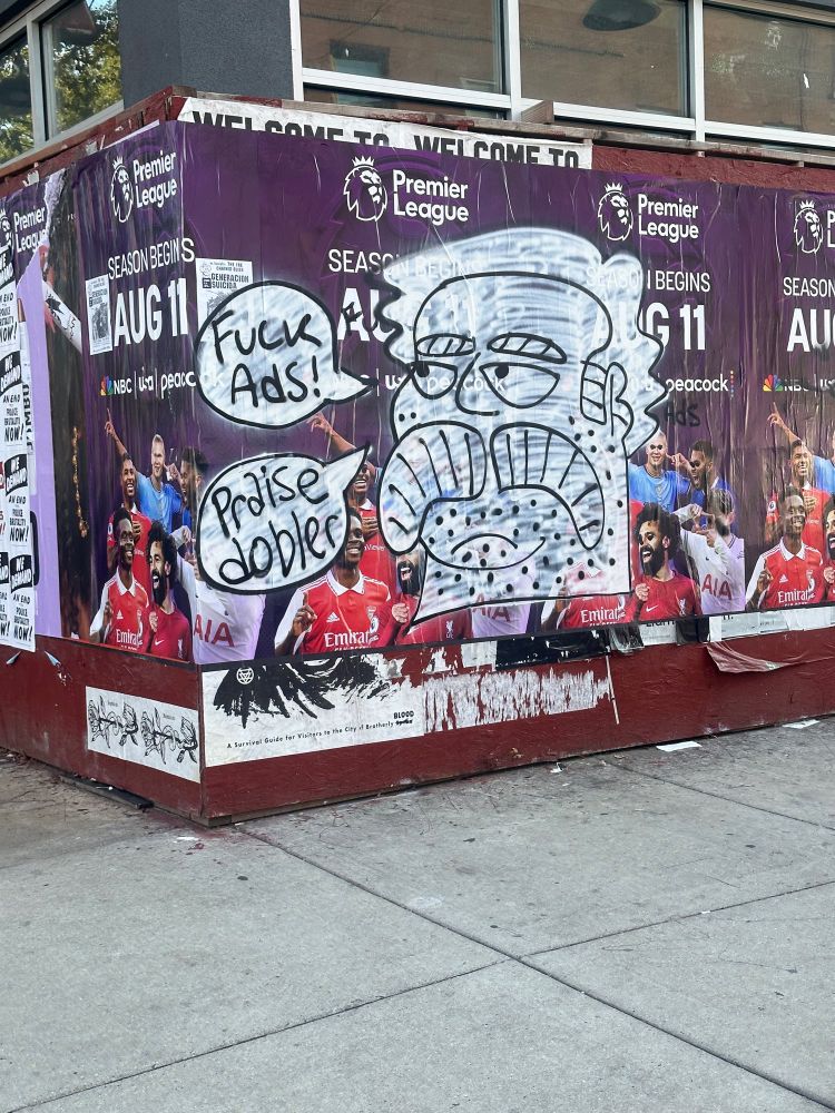 Graffiti of a large man over a fifa ad saying “fuck ads! Praise dobler” I imagine this man is named dobler and we must praise him