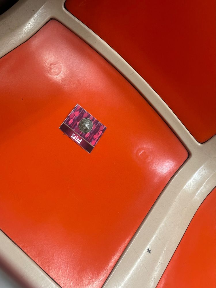 A piece of purple paper on the seat of a supway that has a silver crest of some kind that just says “salad” underneath it. I think it’s a weed thing but it’s also funny