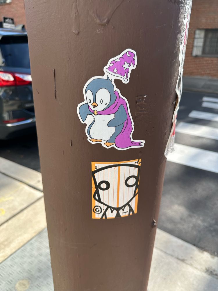 Wizard penguin sticker on a pole and a robot sticker below it