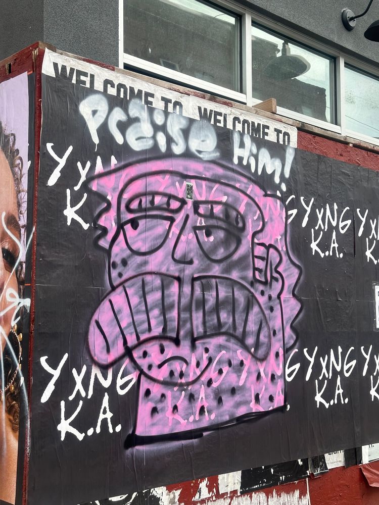 Dobler is back! Praise him! Covering ads! (He is graffiti of a large man with a mustache covering an ad and it says “praise him”)
