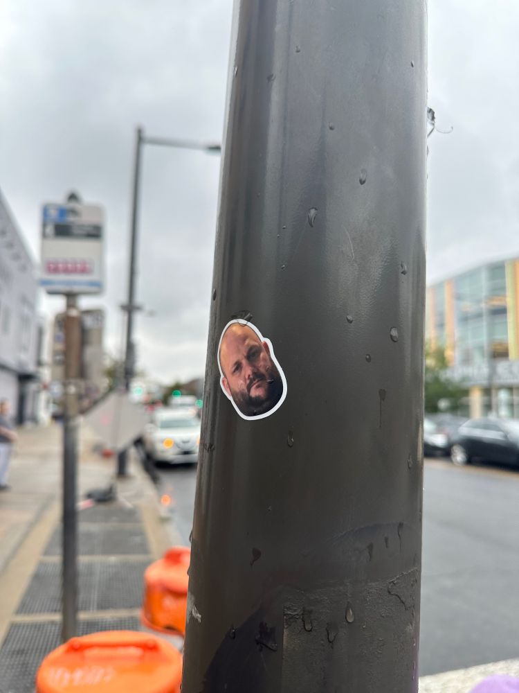 A sticker on a pile of a random human man with a beard and bald head on a pole in philadelphia