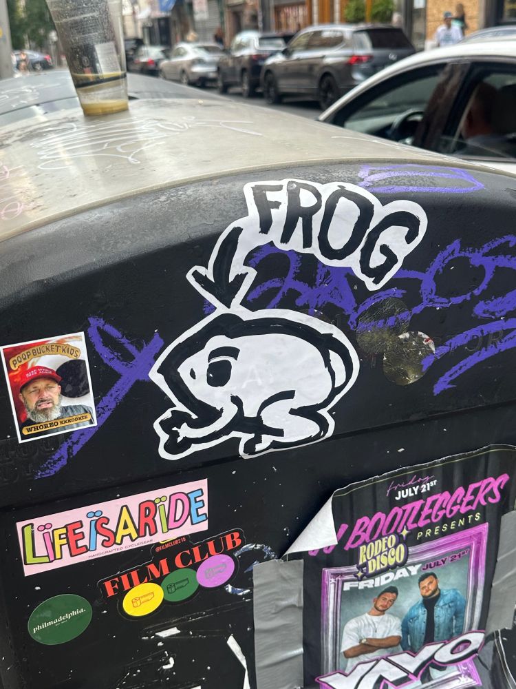 Graffiti of a frog on the side of a trash can with a very helpful arrow pointing at the frog and labeling it frog