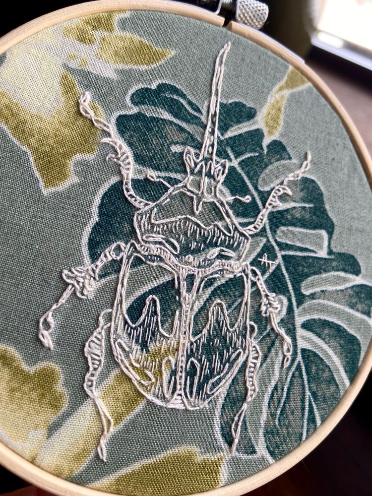embroidery piece depicting a hercules beetle on a botanical background 