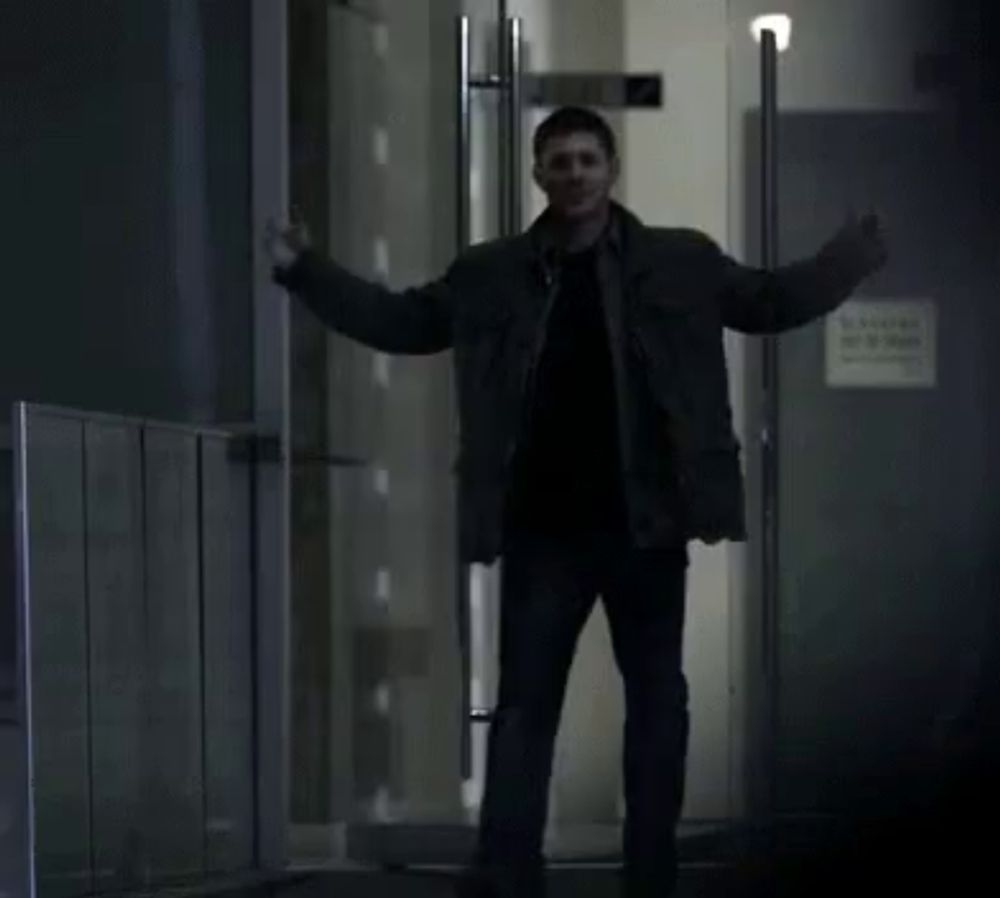 a man is standing in front of a door in a dark room and laughing .