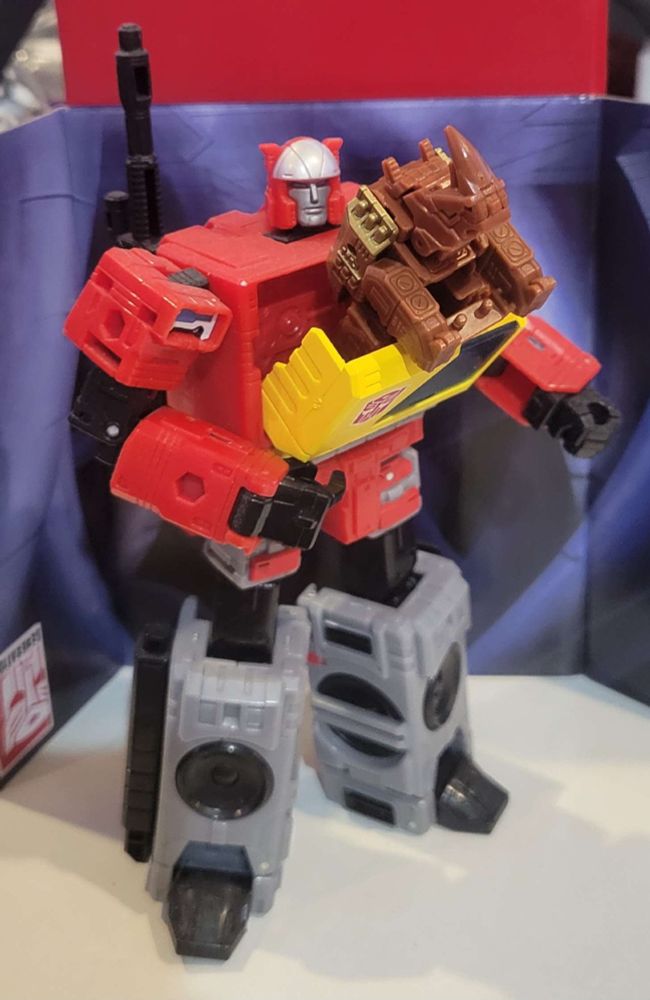 A brown robotic rhino (Titans Return Ramhorn) leaping out of the chest compartment of a red, grey, and yellow robot that turns into a boom box (Kingdom Blaster).