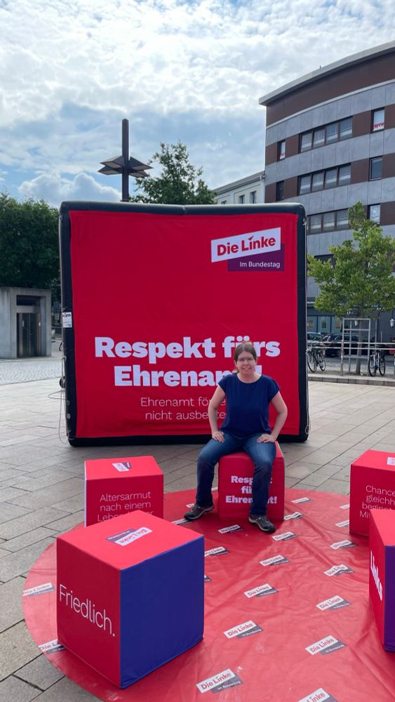 Eine Frau (Sonja) sitzt auf einem bedruckten Würfel, der in einem Sitzkreis steht. Im Hintergrund ist der große Aufblaswürfel auf dem steht "Respekt fürs Ehrenamt.