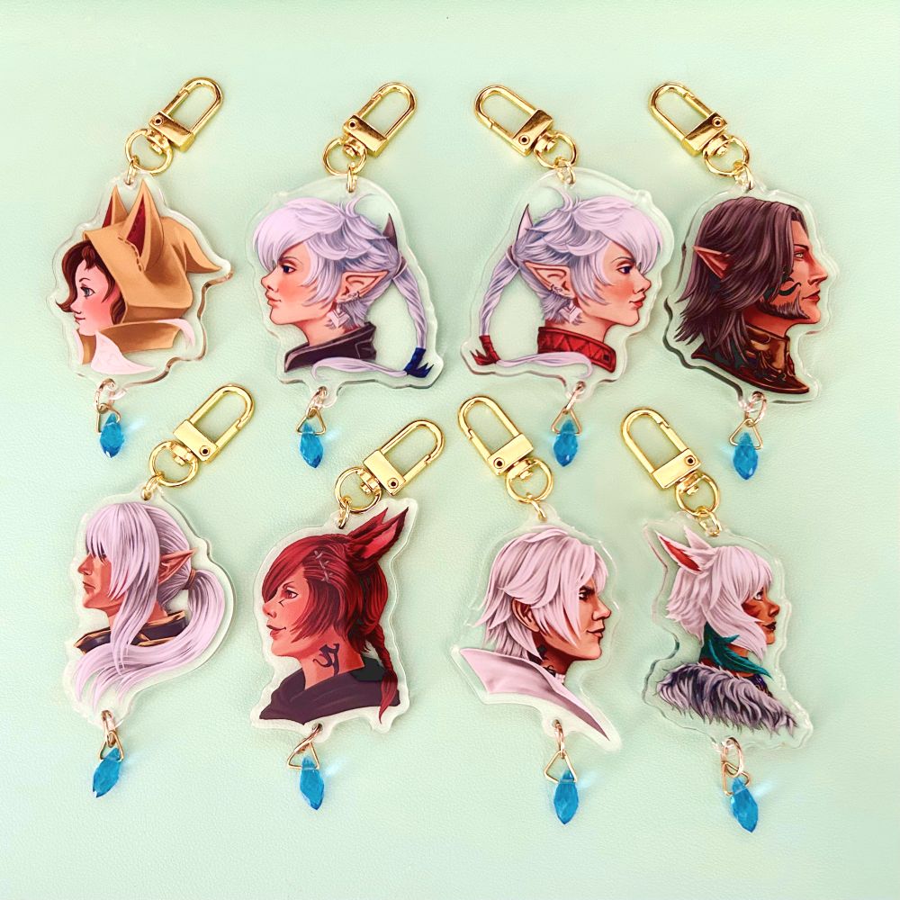Photo of eight keychains with busts of Alphinaud, Alisaie, Estinien, G’raha Tia, Krile, Thancred, Urianger and Y’shtola. Each keychain has a gold clasp and a small blue crystal hanging from the bottom. 