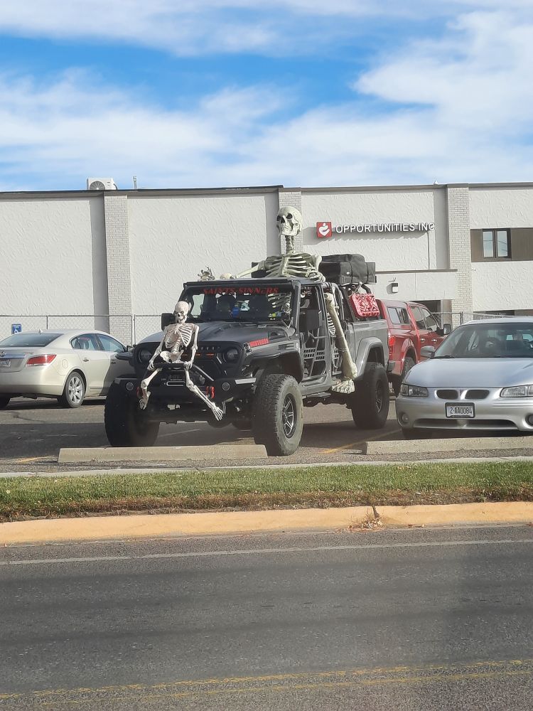 An open top black vehicle that's kind of like a Jeep and a small pickup. In the back sits one of those 12 foot tall skeletons, which still towers over the top, despite the "sitting" position. There is a smaller skelton in thr passenger seat and also attached to the grill on the front of the vehicle.