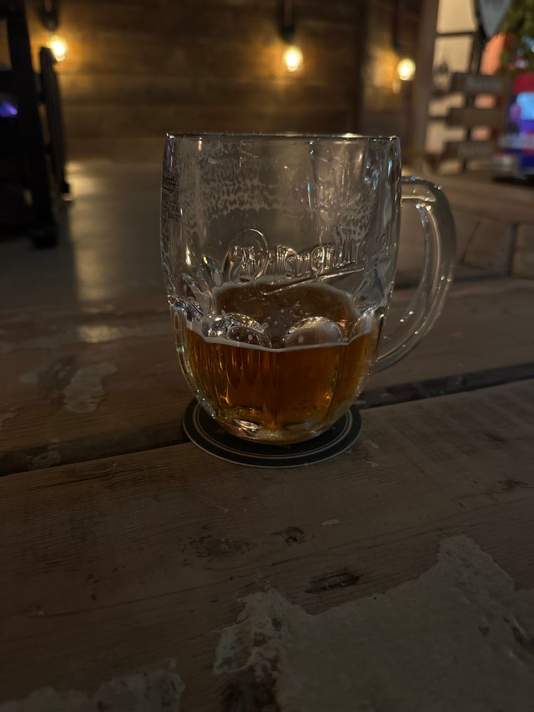 A half-drunk pint of Pilsner Urquell sitting on a rustic table in an atmospherically-lit room.