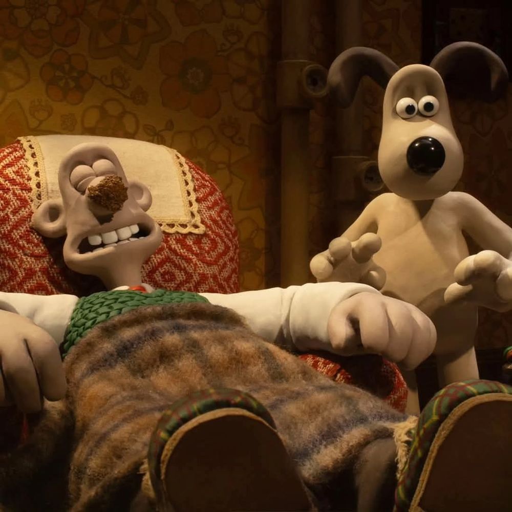 Wallace recostado na cadeira com o nariz inchado, Grommit em pé ao seu lado.