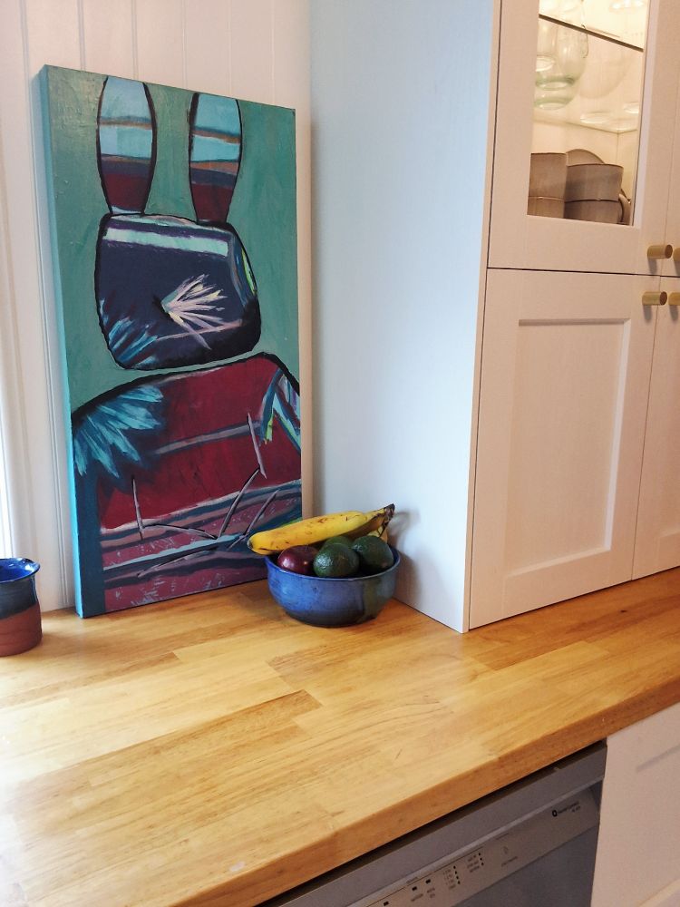 A painting of a bunny leaning on a kitchen counter.