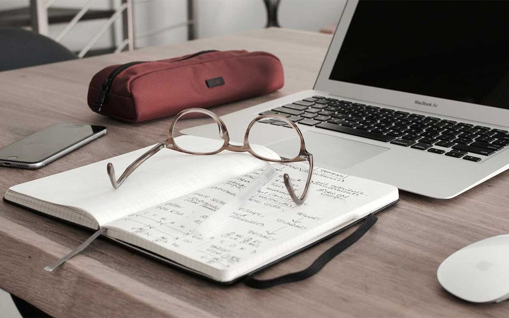 Laptop, notepad, mobile phone and reading glasses on desk