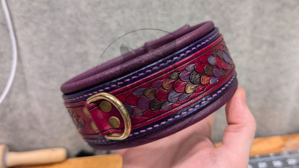 Layered leather, purple-oriented dragonscale collar. Oxblood red top strap with multi-colored purple painted dragonscale tooling with gold and bronze metallic accents, purple back strap, plum purple leather liner, mauve thread, solid brass hardware with matching colored rivets.