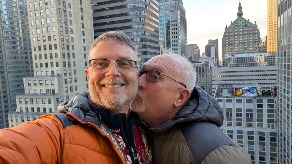 One man kissing his husband in front of the New York skyline.