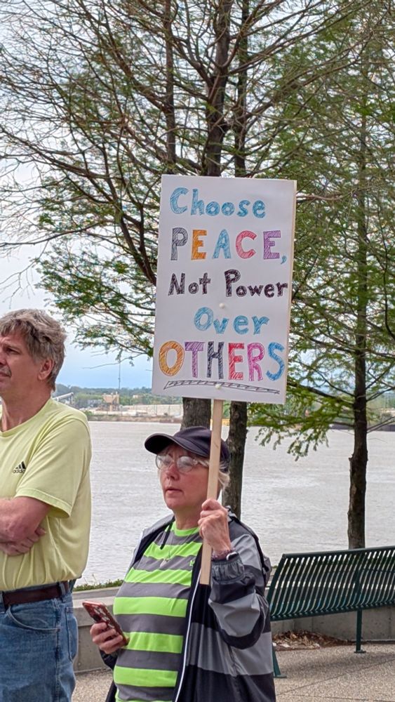 Woman holding a sign the reads "Choose peace not power over others."