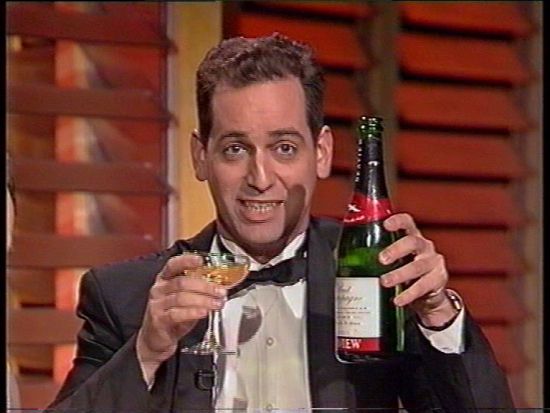 Rob Sitch in a bow tie and tuxedo holding a glass and bottle of champagne 