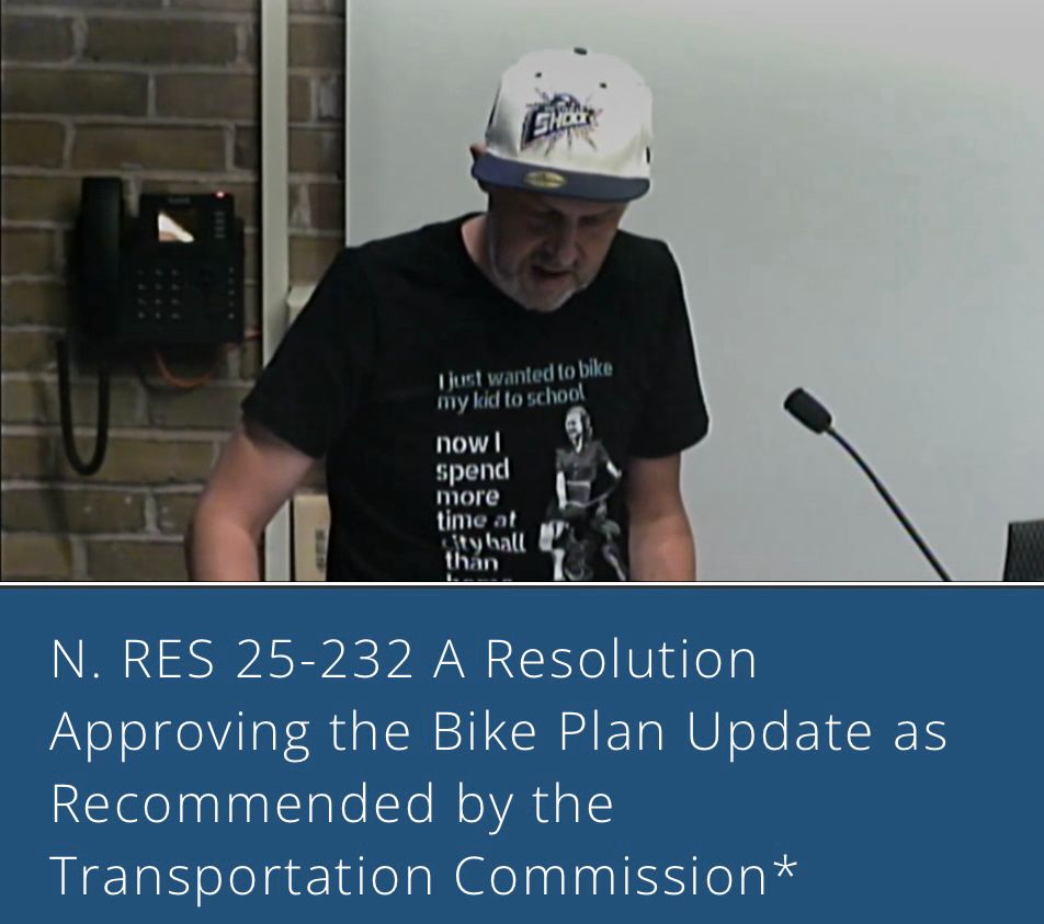 My fellow Bike Walk Oak Park member delivering public comment at a Village Board Meeting wearing a black Rovelo Creative tshirt that reads in white letters “I just wanted to bike my kids to school. Now I spend more time at city hall than at home.”