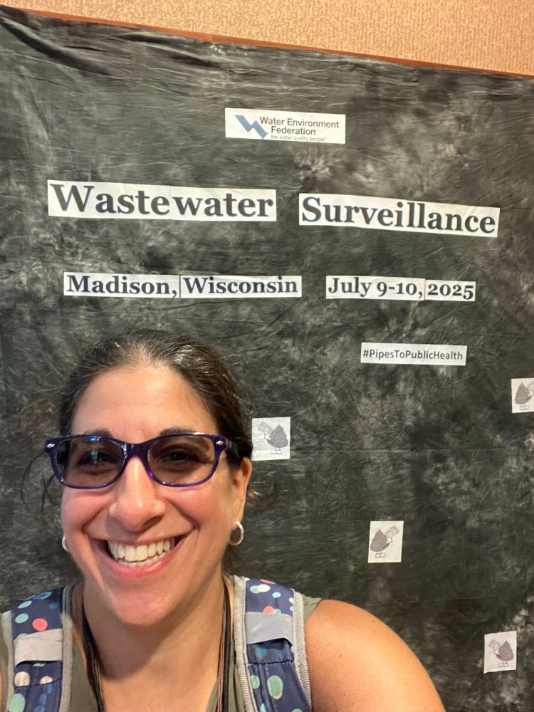 Selfie in front of a wastewater surveillance backdrop with the date (July 9-10), location (Madison, WI), and silly poop emojis with binoculars. 
