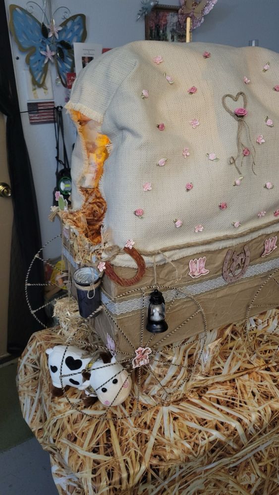 Babydoll riding a rocking horse that is pulling a self made canopy wagon decorated with pink flowers and cowgirl attire. Hand created as a diaper cake/centerpiece for a baby shower.