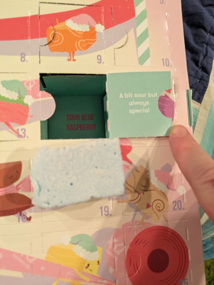 Close up of marshmallow Advent calendar with one door open and a blue marshmallow. The inside of the box says sour blue marshmallow. The door says a bit sour but always special.