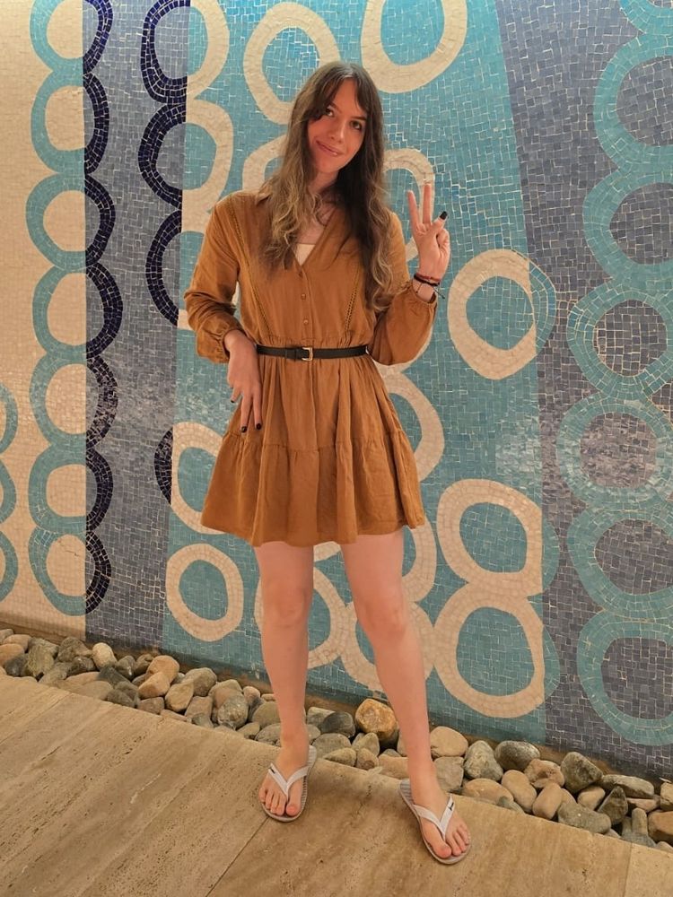 Discord de vestido marrom, cinta preta e chinelos. Ela ta fazendo um piece sign e tentando ser chiq